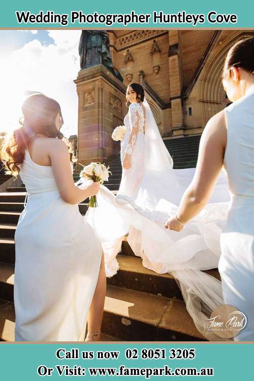 Photo of the Bride smiling on the bridesmaid holding the tail of her wedding gown at the front of the churchHuntleys Cove NSW 2111